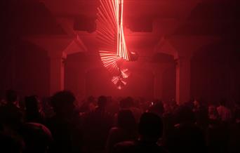 Twisting red neon strip lights in a dark room above a dancing crowd