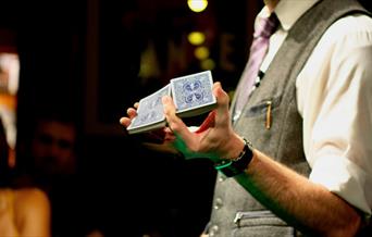 Person with grey waistcoat holding a deck of cards