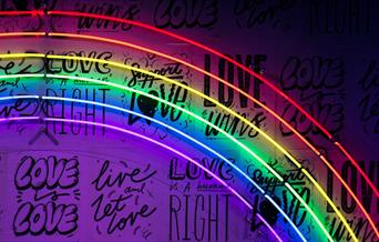 A neon rainbow sign with black writing behind it