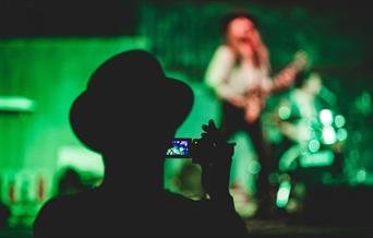 Person recording video of a person playing guitar onstage