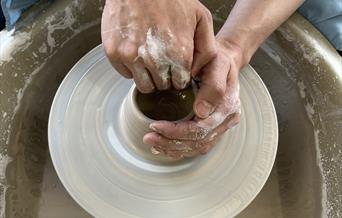 An overhead shot of someone throwing a pot on a potter's wheel