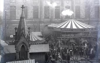 A black and white photo of a fun fair in a town centre
