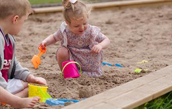 two children playing in a sand pit with brightly coloured buckets and spades