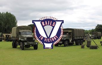 Several classic military vehicles parked in a field, with Rails To Victory branding over the top