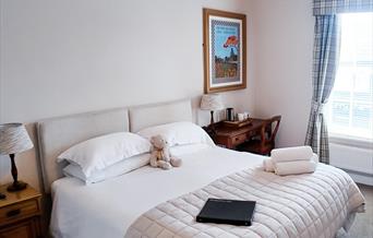 Bedroom with double bed, bedside tables, towels on the bed, and a teddy sitting between the pillows