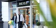 A man and a woman leave the Reiss store at McArthurGlen West Midlands, with smiles on their faces and shopping bags in their hands