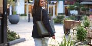 A shopper looks over her shoulder and smiles at the camera, as she walks along one of the malls at McArthurGlen West Midlands