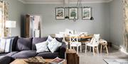 A lounge area of a cottage, with dining table and chairs in the background and a comfortable corner sofa in front