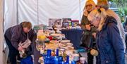 A  stall under a white gazebo displaying assorted household items, including blue glassware, ceramic plates, bowls, cups, and jars. Several people bro