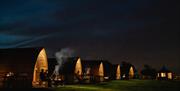 A group of wooden cabins lit up at night with people sitting outside having a BBQ
