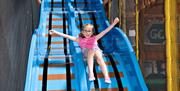 A girl zooms down a blue slide with her arms in the air