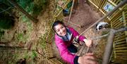 An intrepid visitor climbs a rope ladder and looks at the camera at a high ropes course