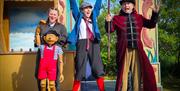three people on stage in costume dress. One person is holding a wooden puppet called Pinocchio