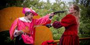 image A: two people in costume dress acting out a fighting seen from the musketeers using pretend pistols 
Image B: two people in costume dress acting