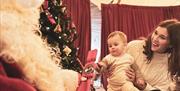 A mum and baby with Santa, with a Christmas Tree in the background