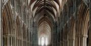 An photograph of the interior of Lichfield Cathedral in natural light, taken looking down the nave of the cathedral with the window glowing at the end