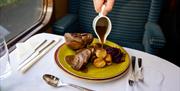 Someone pours gravy onto a roast dinner, on board a train