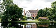 Image shows the team at the Moat House preparing the banks of the lake for an outdoor wedding. Seen from across the lake, with pretty reflections of t