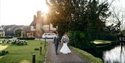 Image shows a couple walking down the path after their wedding, as the sun begins to set behind the farm house