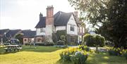 Image shows the farmhouse at The Moat House on a sunny day, looking over from beside the pool at the daffodils and picnic benches