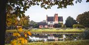 Image shows the lake, tables and farmhouse at The Moat House on an Autumnal day