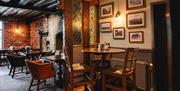 Image shows the lounge bar area of The Moat House, with a huge stone fireplace, oak beams on the ceiling, and a variety of tables and chairs