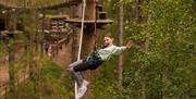 An adventurous female visitor balances on a rope at a high ropes course in a forest