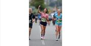 Runners crossing a city centre finish line, raising arms in celebration during a road race event.