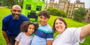 Visitors pose for a selfie beside a giant Minecraft Creeper in front of a historic building.