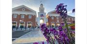 Outlet shopping centre entrance with clock tower and flowers in foreground.