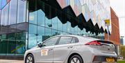 A gleaming grey/silver taxi parked outside a colourful building