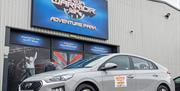 A taxi parked outside a warehouse with a Ninja Warrior UK Adventure Park sign above some big glass doors