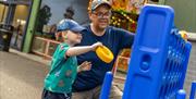 A boy and his grandad play on a giant Connect 4, in a play area in front of a fairground
