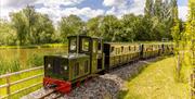 A heritage steam train chugs along a track beside a lake, on a sunny day