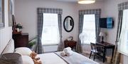 A large bedroom with bed, plasma screen TV, desk, fan and other furnishings