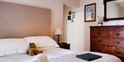 A bed with teddy, towels, and a leather folder on it. There is a large mirror on the wall, and a tall wooden chest of drawers.