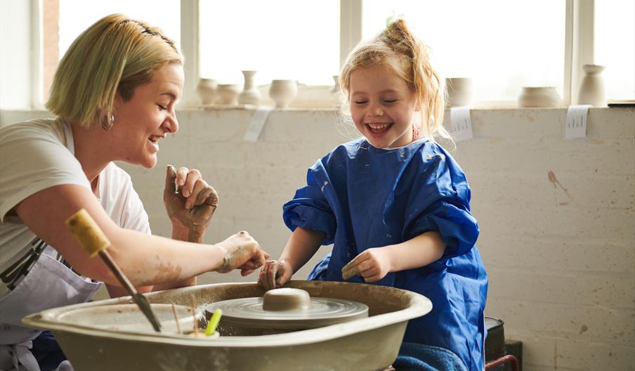 A mum with her daughter, looking at some clay spinning on a potters' wheel A mum with her daughter, looking at some clay spinning on a potters' wheel